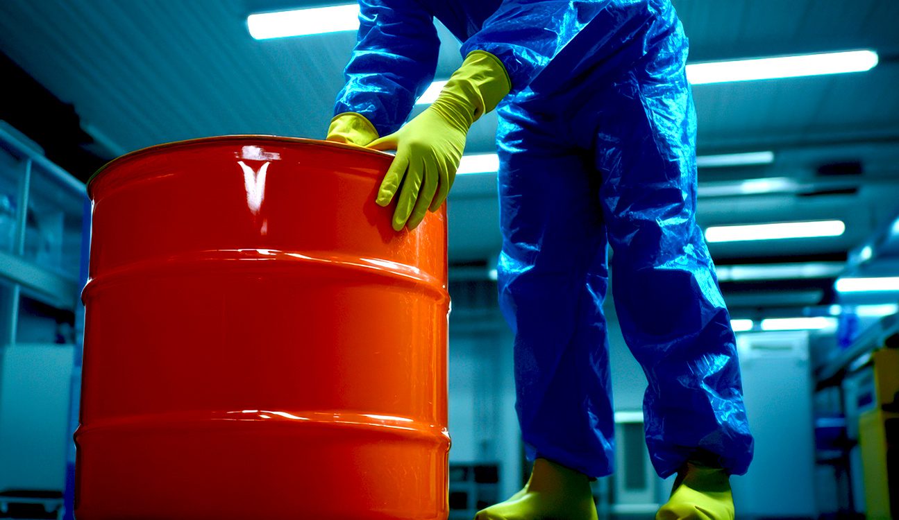 Profissional com traje de proteção ao lado de um barril de produto químico